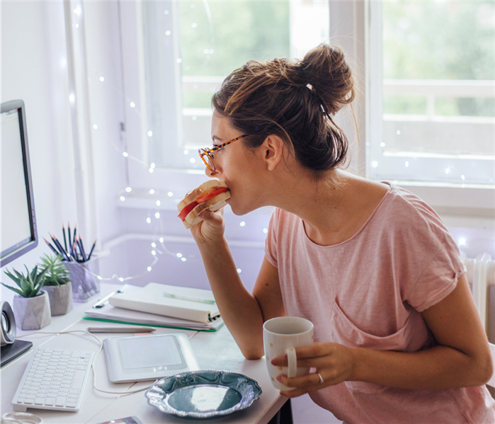 Woman dressed down eating a sandwich at her desk in her home