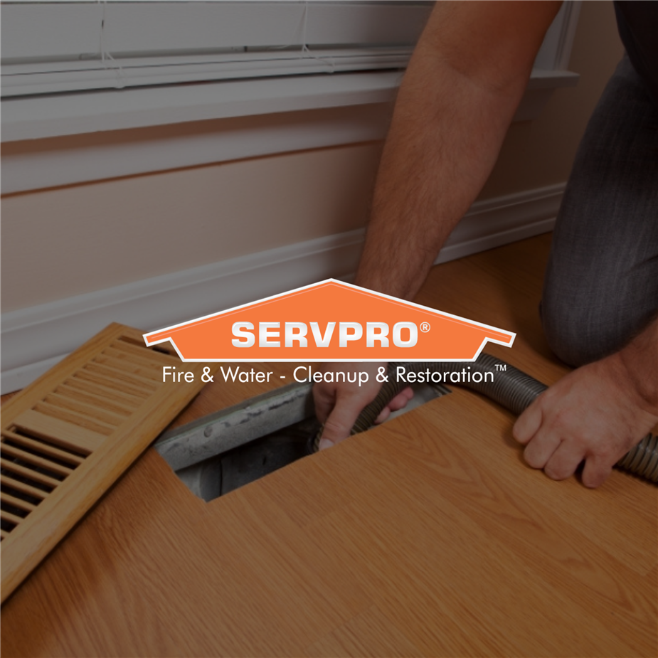 Man kneeling with a tube down into the air ducts with Servpro logo over the photo